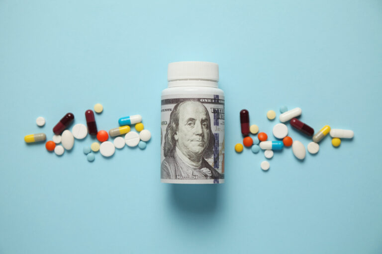 Money and pills of different colors on blue background. Rising cost of health care.